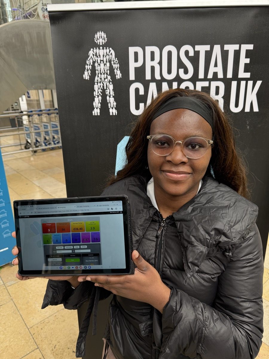 CKT brand ambassador holding a tablet showing the Engaging donation app at a Prostate Cancer UK stand.